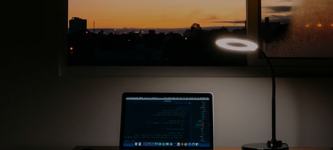 A laptop on a desk with a lamp in the dark